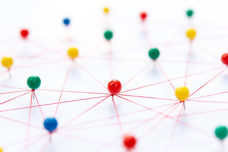 Colorful pins connected by a network of red threads on a white background, representing concepts of networking, connectivity, and relationships.
