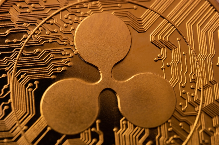 Close-up view of a Ripple XRP cryptocurrency coin, showcasing the detailed circuitry pattern embossed on its golden surface.
