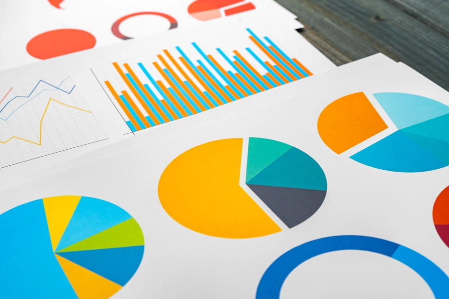 Alt text: "Printed sheets with colorful charts including pie charts, bar graphs, and line graphs laid out on a wooden table, depicting data visualization for analysis.