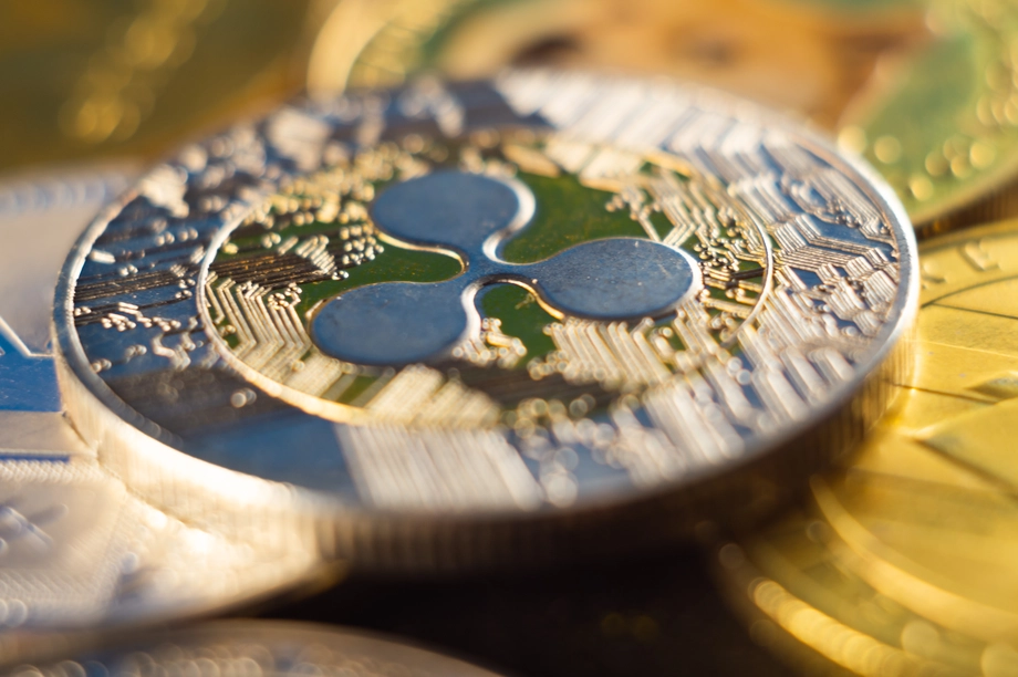 Close-up of a Ripple XRP cryptocurrency coin with intricate circuitry design, resting among other blurred coins, highlighting the detail of digital currency.