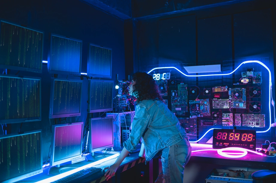A woman standing in a neon-lit server room, monitoring data on multiple screens, depicting network management and cybersecurity.