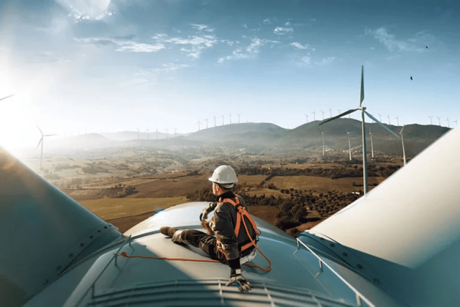 turbine technician sitting on turbine overlooking view of valley and mountains in the distance