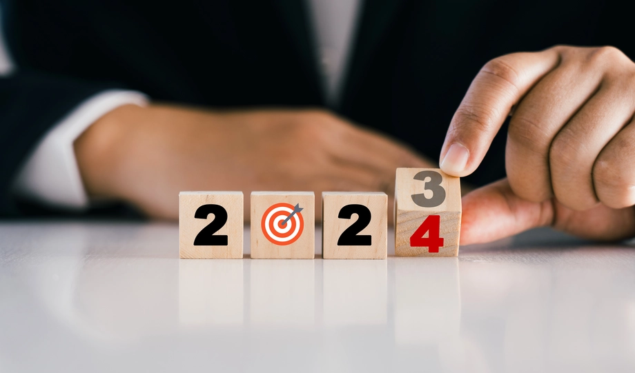 Business person aligning wooden blocks with numbers and target symbol, changing '2023' to '2024', illustrating goal setting or strategic planning for the new year.