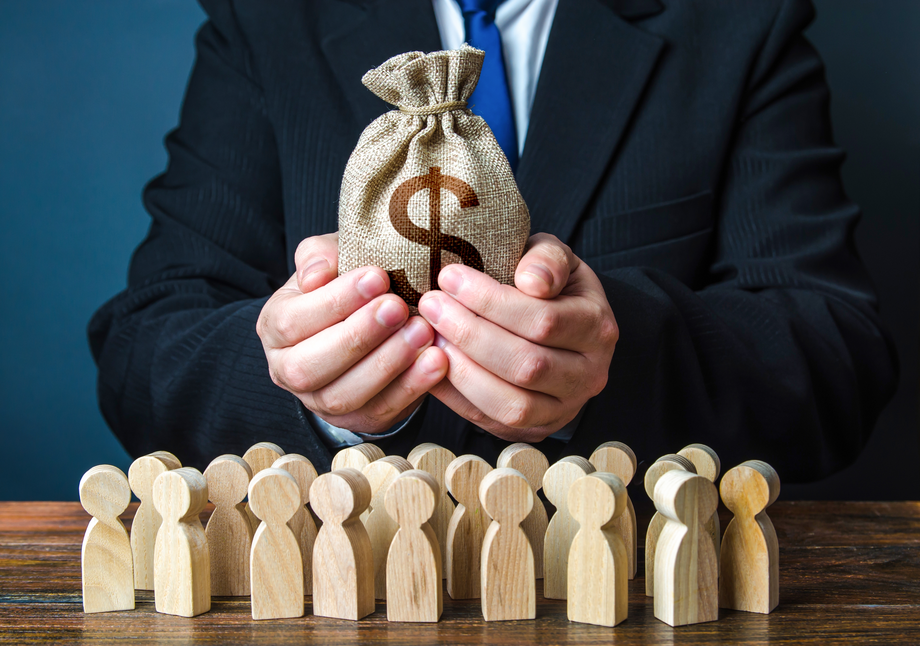Businessperson presenting a money bag in front of a lineup of wooden figures, symbolizing investment in private equity